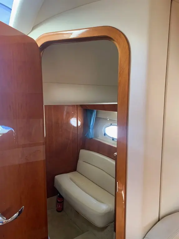 View into a yacht interior featuring a beige leather sofa, wooden paneling, and a fire extinguisher near the entryway.